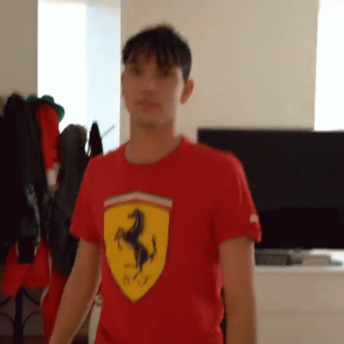 A Young Man Wearing A Red Ferrari Shirt Is Standing In Front Of A Television . GIF