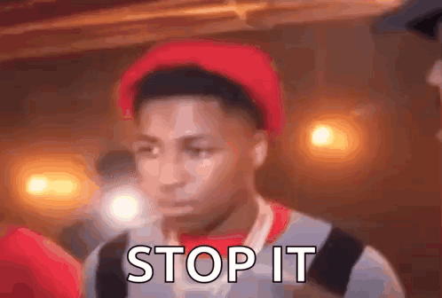 A Young Man Wearing A Red Hat And A Backpack Is Standing In Front Of A Crowd . GIF