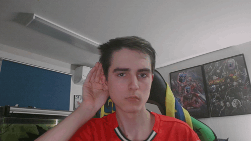 A Young Man Wearing A Red Shirt Is Covering His Ear With His Hand GIF