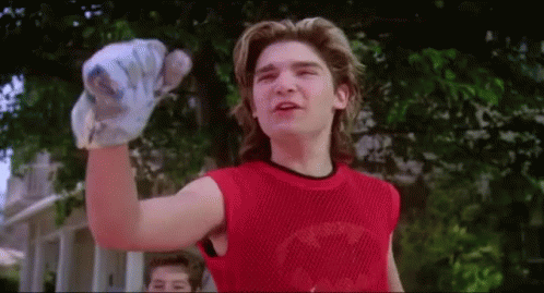 A Young Man Wearing A Red Tank Top Is Holding A Baseball Bat In His Hand . GIF