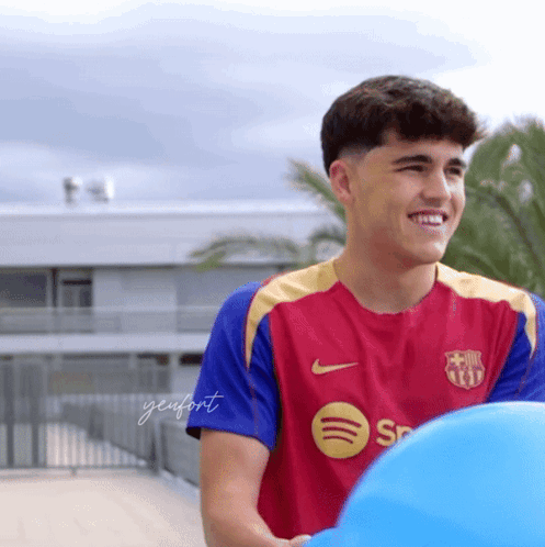 A Young Man Wearing A Spotify Shirt Smiles While Holding A Blue Ball GIF