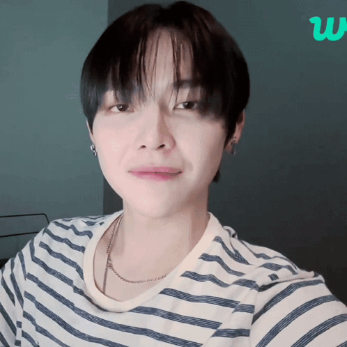 A Young Man Wearing A Striped Shirt And A Necklace Looks At The Camera GIF