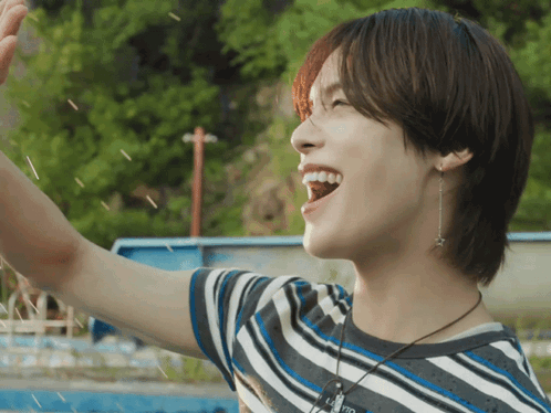 A Young Man Wearing A Striped Shirt And A Necklace With A Star On It Is Smiling GIF
