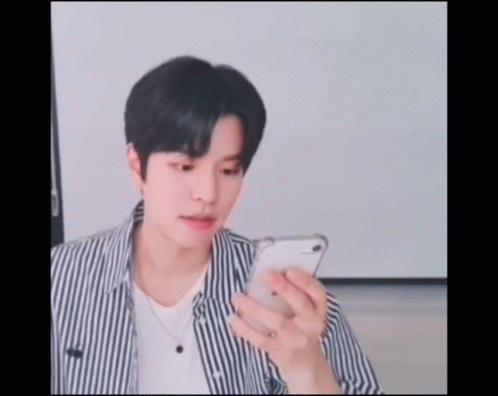 A Young Man Wearing A Striped Shirt Is Looking At His Phone GIF