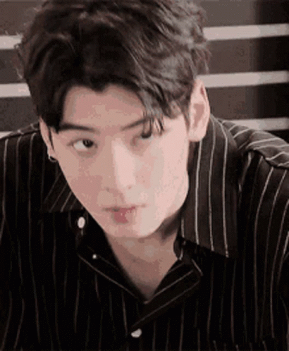 A Young Man Wearing A Striped Shirt Is Looking At The Camera . GIF
