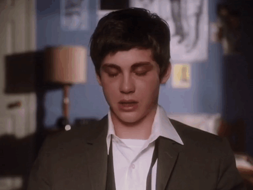 A Young Man Wearing A Suit And Tie Is Looking Down With His Eyes Closed GIF