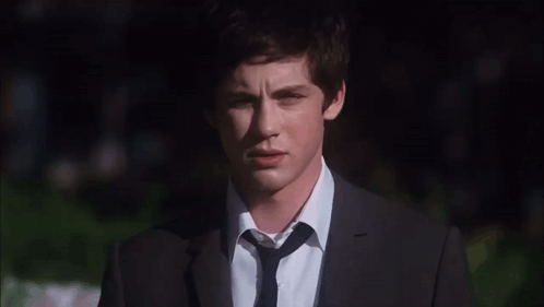 A Young Man Wearing A Suit And Tie Looks At The Camera GIF