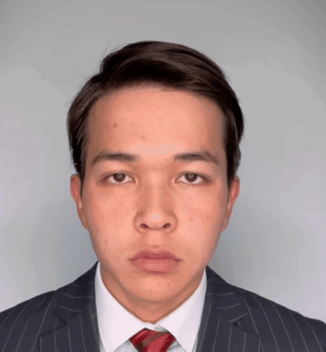 A Young Man Wearing A Suit And Tie Looks At The Camera GIF