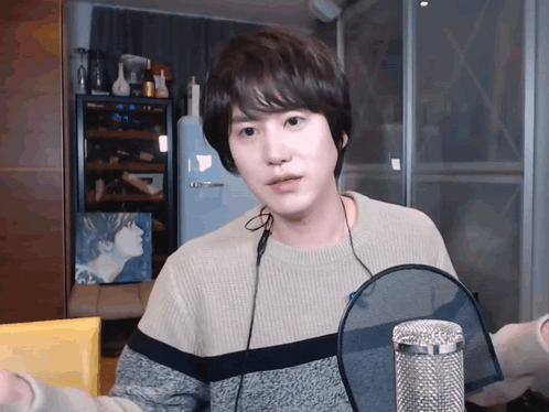 A Young Man Wearing A Sweater And Headphones Is Standing In Front Of A Microphone GIF
