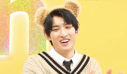 A Young Man Wearing A Sweater And Tie With Teddy Bear Ears On His Head Is Smiling . GIF