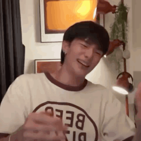 A Young Man Wearing A T-Shirt With The Word Bee On It Is Laughing While Standing In A Room . GIF