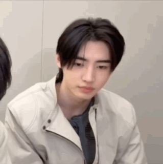 A Young Man Wearing A White Jacket And A Blue Shirt Is Looking At The Camera . GIF