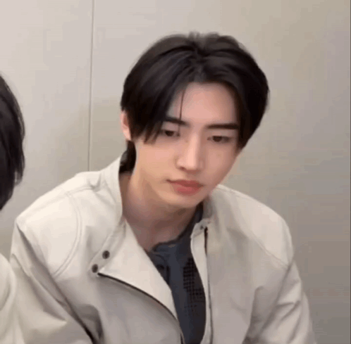 A Young Man Wearing A White Jacket Is Looking At The Camera . GIF