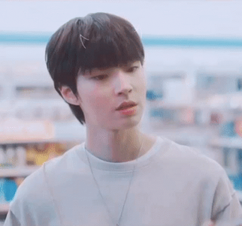 A Young Man Wearing A White Shirt And A Necklace Is Standing In A Store . GIF