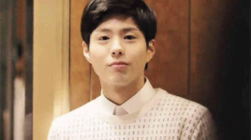 A Young Man Wearing A White Shirt And Sweater Is Looking At The Camera . GIF