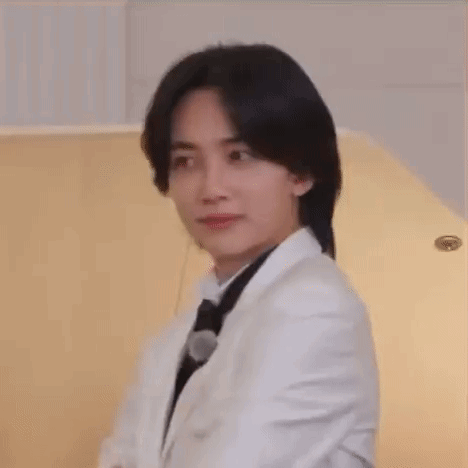 A Young Man Wearing A White Suit And Black Tie Is Sitting In Front Of A Piano . GIF
