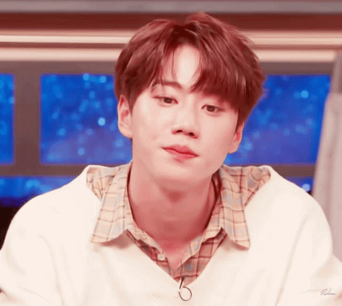 a young man wearing a white sweater and plaid shirt looks to the side