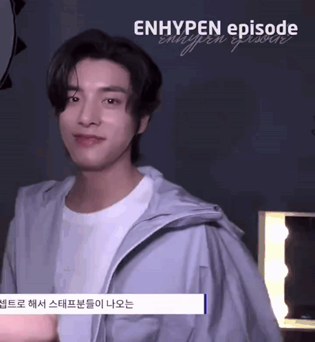 A Young Man Wearing A White T-Shirt And A Gray Jacket Is Standing In Front Of A Mirror And Smiling . GIF