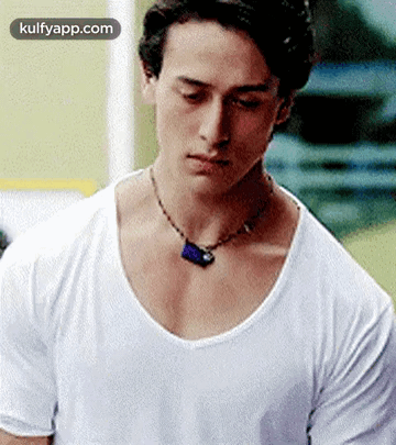 A Young Man Wearing A White T-Shirt And A Necklace Is Looking Down . GIF