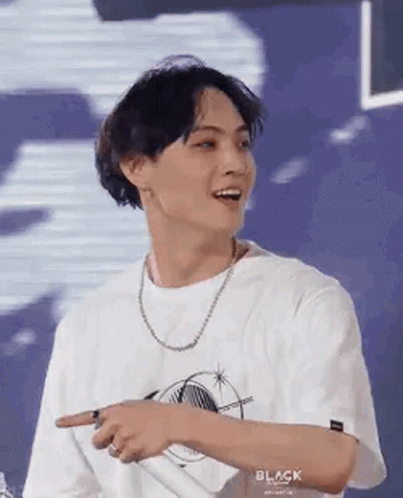 A Young Man Wearing A White T-Shirt And A Necklace Is Pointing At Something With His Finger . GIF
