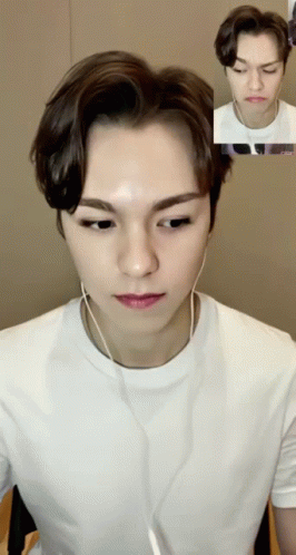 A Young Man Wearing A White T-Shirt And Earbuds Looks At The Camera While Making A Funny Face GIF