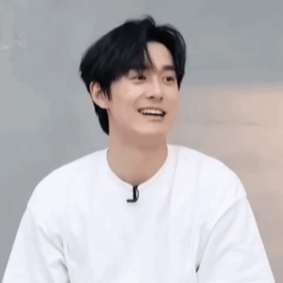 A Young Man Wearing A White T-Shirt Is Smiling And Looking At The Camera . GIF