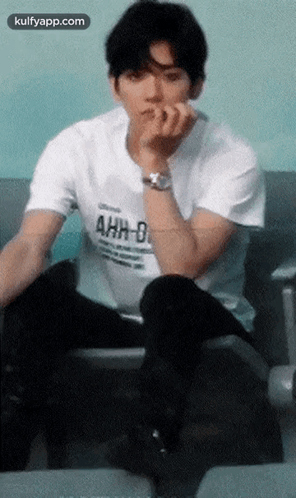 A Young Man Wearing A White T-Shirt That Says Ahh-D Is Sitting On A Chair GIF