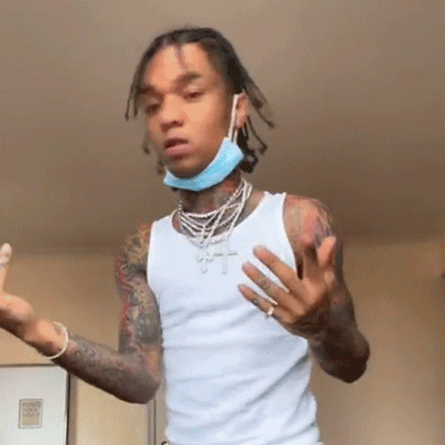 A Young Man Wearing A White Tank Top And A Blue Face Mask Is Standing In A Room . GIF