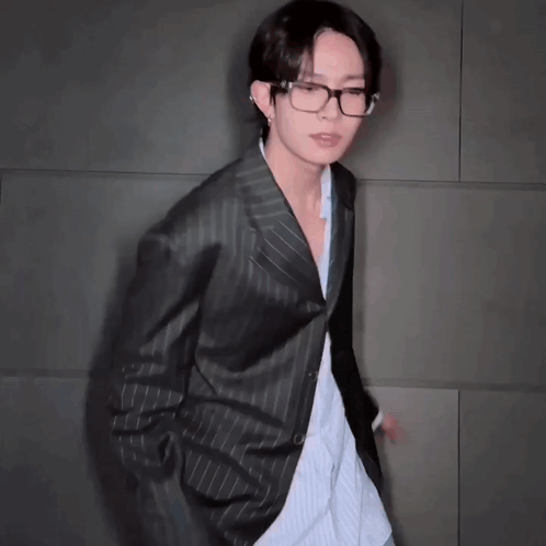 A Young Man Wearing Glasses And A Black Jacket Is Dancing . GIF