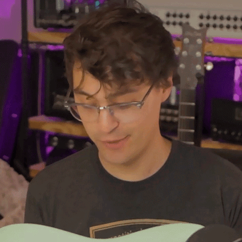 A Young Man Wearing Glasses And A Black Shirt Is Playing A Guitar GIF