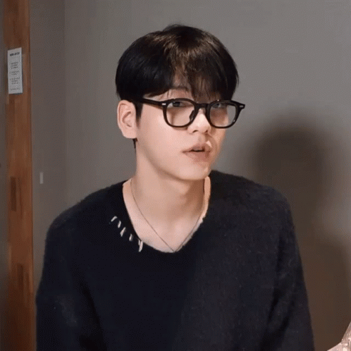 A Young Man Wearing Glasses And A Black Sweater Is Standing In Front Of A Sign That Says ' No Smoking ' GIF
