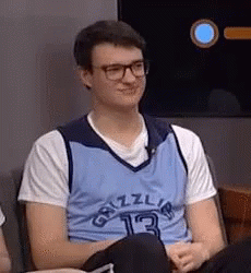 A Young Man Wearing Glasses And A Blue Grizzlies Jersey Is Sitting In A Chair . GIF