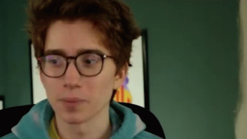 A Young Man Wearing Glasses And A Blue Hoodie Is Sitting In A Chair . GIF