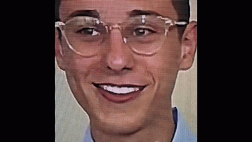 A Young Man Wearing Glasses And A Blue Shirt Is Smiling . GIF