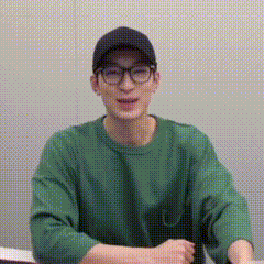 A Young Man Wearing Glasses And A Green Sweater Is Sitting At A Table . GIF