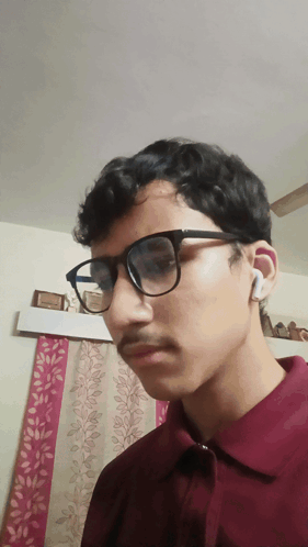 A Young Man Wearing Glasses And A Maroon Shirt Is Looking At The Camera GIF