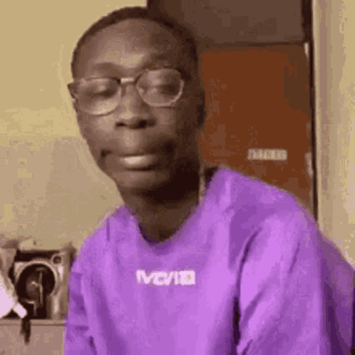 A Young Man Wearing Glasses And A Purple Shirt Is Making A Face . GIF