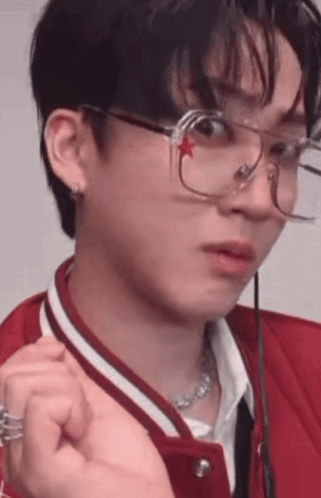 A Young Man Wearing Glasses And A Red Jacket Is Making A Face . GIF