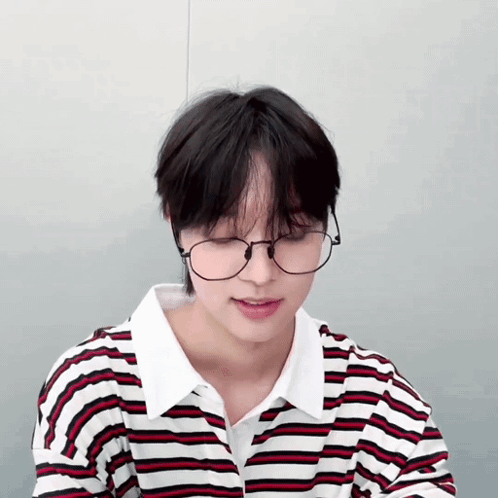A Young Man Wearing Glasses And A Striped Shirt Looks Down GIF