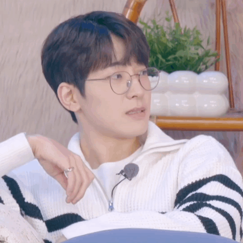 A Young Man Wearing Glasses And A Striped Sweater Holds A Pen GIF