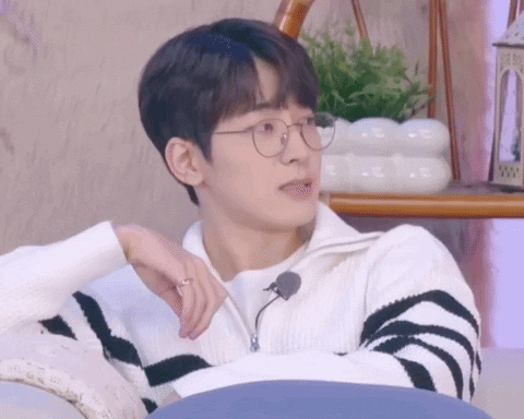 A Young Man Wearing Glasses And A Striped Sweater Is Sitting On A Couch With His Hand On His Chin . GIF