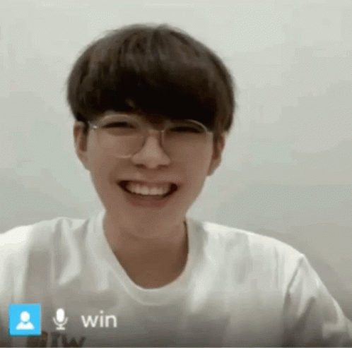 a young man wearing glasses and a white shirt is smiling in front of a microphone that says win