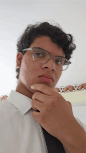 A Young Man Wearing Glasses And A White Shirt Looks At The Camera GIF