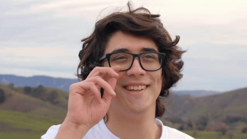 A Young Man Wearing Glasses And A White Shirt Smiles At The Camera GIF