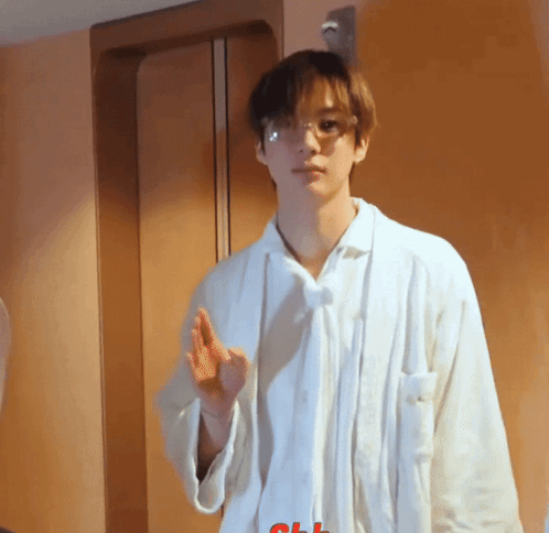 A Young Man Wearing Glasses And A White Shirt Stands In Front Of A Door GIF