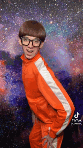 A Young Man Wearing Glasses And An Orange Jacket Is Dancing In Front Of A Galaxy . GIF