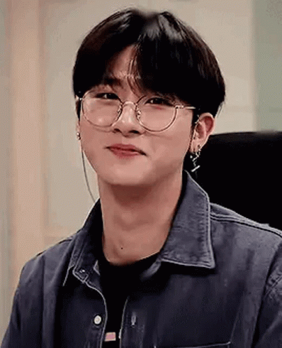 A Young Man Wearing Glasses And Earrings Is Smiling . GIF