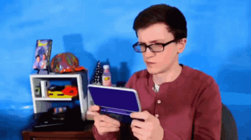 A Young Man Wearing Glasses Is Holding A Nintendo 3Ds GIF