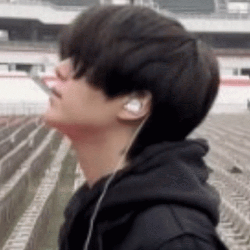 A Young Man Wearing Headphones And A Black Hoodie Is Smoking A Cigarette . GIF