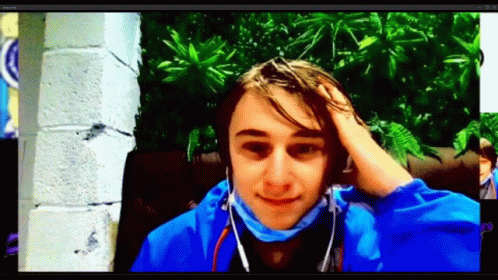 A Young Man Wearing Headphones And A Blue Jacket Holds His Hand To His Forehead GIF